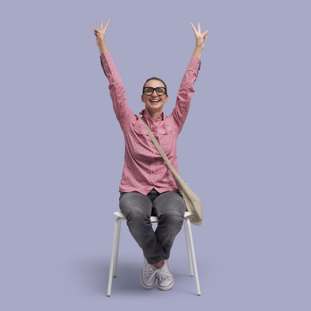 Une femme joyeuse assise sur une chaise et célébrant avec les bras levés