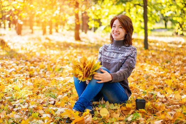 Femme joyeuse assise sur des feuilles jaunes