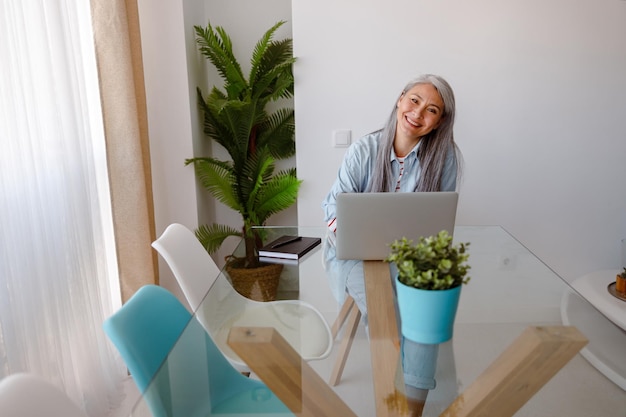 Femme joyeuse assise à la table avec un ordinateur portable à la maison