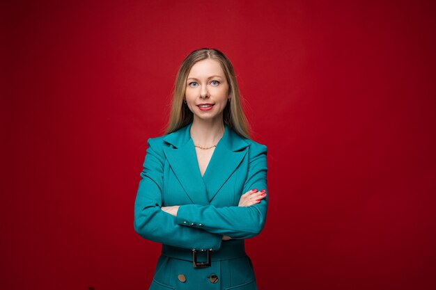 Femme joyeuse aux cheveux blonds en costume de bureau sourit, photo isolée sur fond rouge