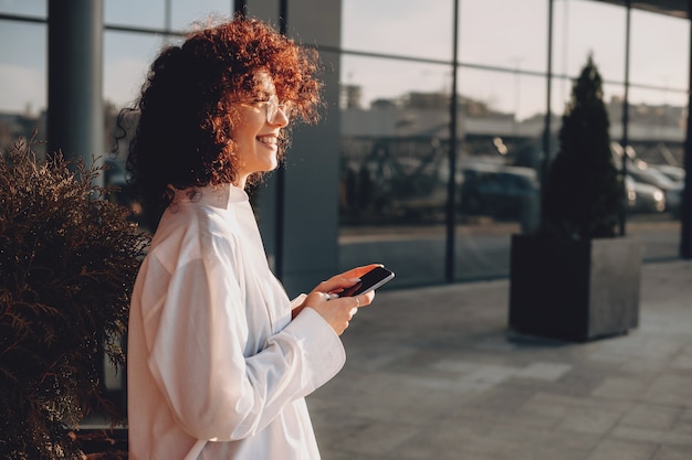 Femme joyeuse aux cheveux bouclés et lunettes discute avec quelqu'un tout en regardant ailleurs