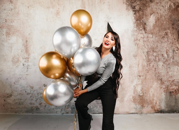 Une femme joyeuse avec des ballons rit une jeune brune aux cheveux longs célèbre son anniversaire des ballons à l'hélium