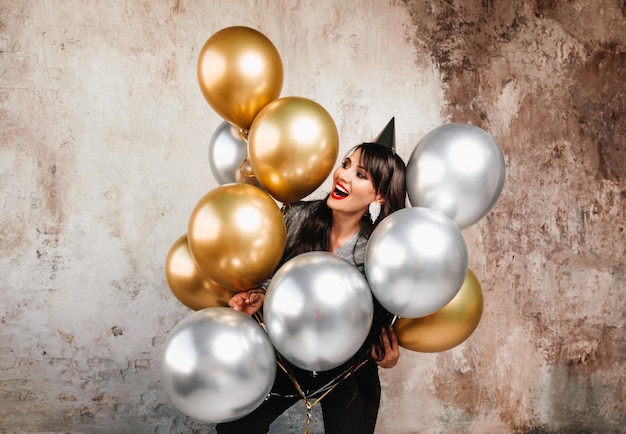 Une femme joyeuse avec des ballons rit une jeune brune aux cheveux longs célèbre son anniversaire des ballons à l'hélium