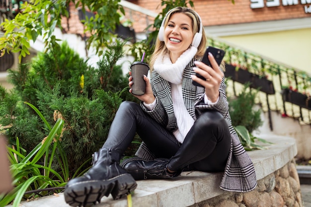 Une femme joyeuse de bonne humeur écoute de la musique via des écouteurs de téléphone et boit du café tout en