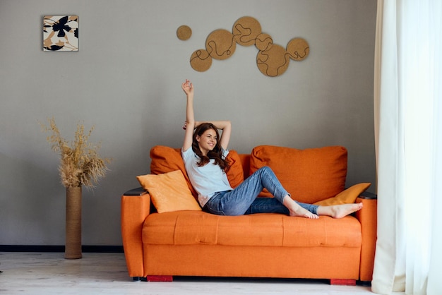Femme joyeuse sur le canapé orange dans la salle de repos posant inchangée