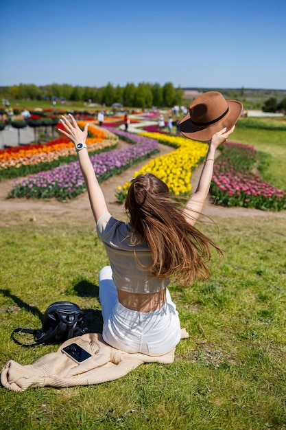Femme joyeuse avec un chapeau de paille assis entre un champ de tulipes en serre