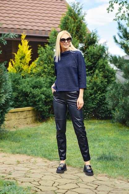 Femme joyeuse en chemisier tricoté et pantalon en cuir dans l'allée du jardin