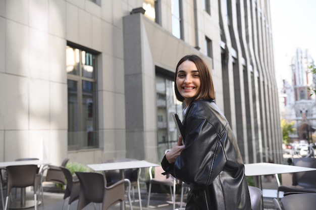 Femme joyeuse confiante, homme d'affaires, pigiste, entrepreneur, rédacteur tenant un ordinateur portable dans ses mains et regardant la caméra sur fond d'immeubles de grande hauteur d'entreprise de bureau moderne