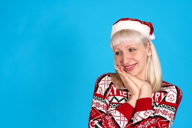 Femme joyeuse dans un pull de Noël et un chapeau de Père Noël sur un fond bleu