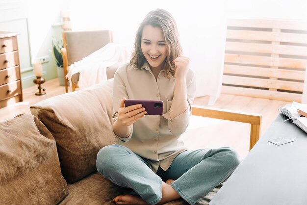 Une femme joyeuse du millénaire, la bouche ouverte, absorbée par son téléphone, jouant à des jeux mobiles, lisant des messages.