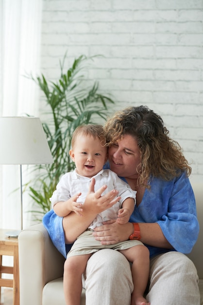 Femme joyeuse embrassant son adorable petit garçon quand ils sont assis sur un canapé dans le salon