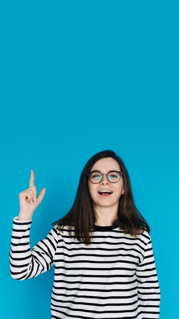 Femme joyeuse excitée en pull rayé avec des lunettes pointant vers le haut Modèle féminin énergique Gesturin