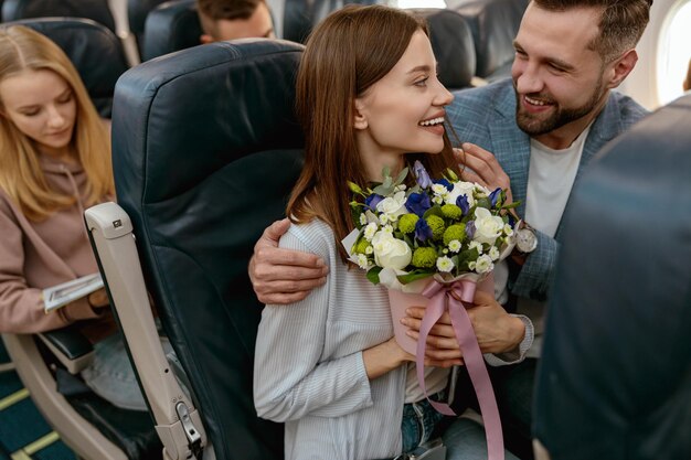 Femme joyeuse avec des fleurs voyageant avec son mari en avion