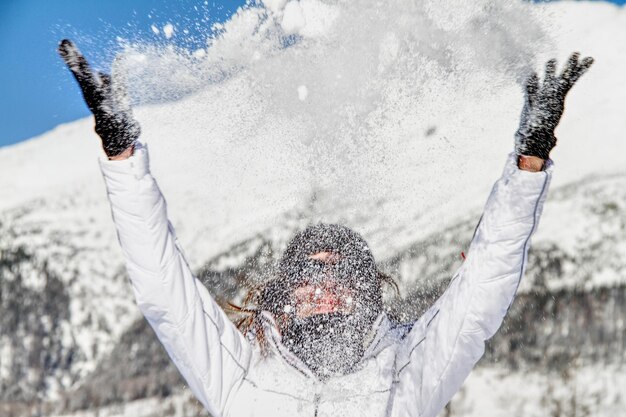 Photo une femme joyeuse jetant de la neige alors qu'elle se tient contre les montagnes