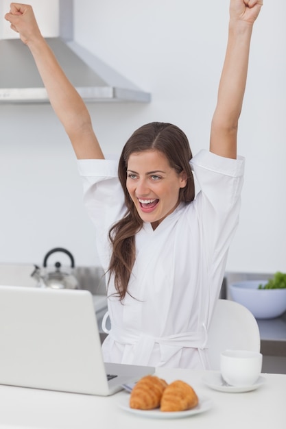 Femme joyeuse levant les bras tout en utilisant un ordinateur portable