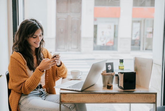 Femme joyeuse, naviguant sur smartphone au café