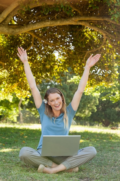 Femme joyeuse avec ordinateur portable, levant les mains au parc