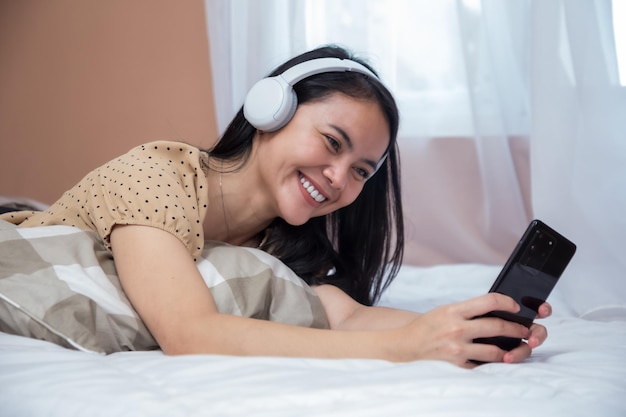 Femme joyeuse portant des écouteurs et tenant un téléphone portable souriant sur le lit