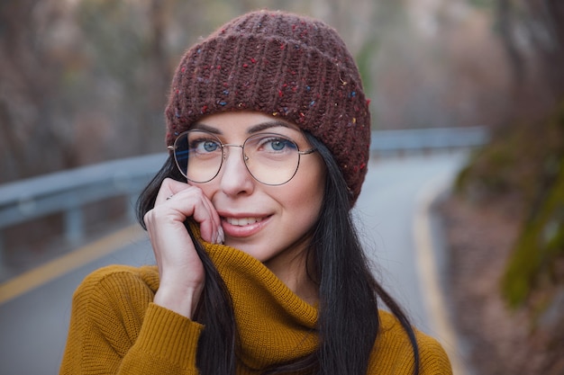 Une femme joyeuse et positive profite de l'automne dans un parc ou dans les bois, porte un pull et un chapeau jaunes, des lunettes. Humeur heureuse hipster girl à la fin de l'automne road trip en forêt