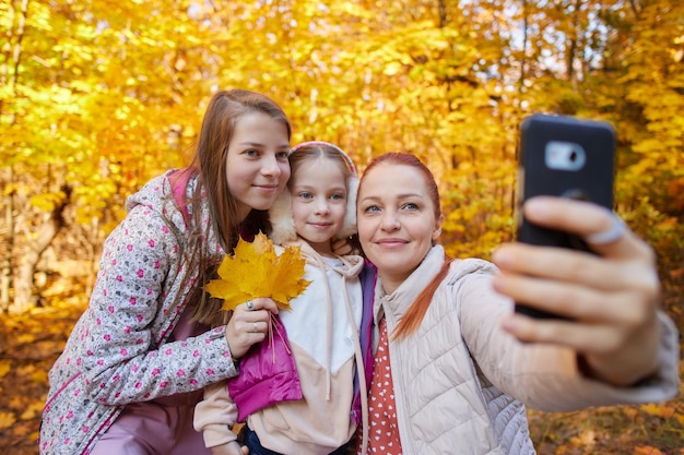 Une femme joyeuse prend des selfies avec ses filles dans un parc d'automne photos de famille de gens heureux