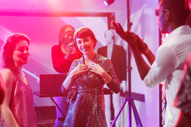 Une femme joyeuse riant et regardant la caméra tout en dansant avec des amis dans une discothèque de boîte de nuit. Une fille heureuse souriante s'amusant sur la piste de danse dans un club avec des projecteurs.