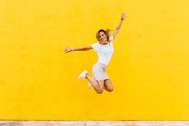 Une femme joyeuse sautant contre un mur jaune