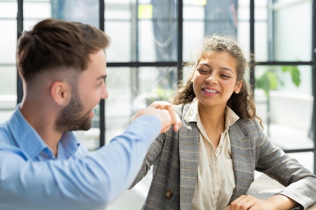 Femme joyeuse se cognant le poing avec un collègue masculin concluant un accord de coopération