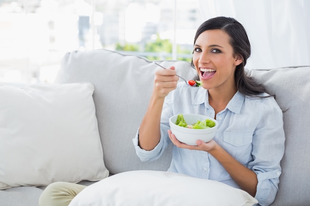 Femme joyeuse se détendre sur le canapé en mangeant une salade