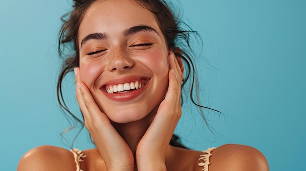 Une femme joyeuse souriant à la caméra et serrant les mains sous la joue tout en faisant semblant de dormir sur un fond bleu