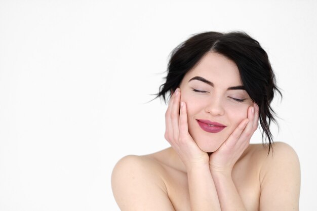 femme joyeuse souriante tenant la tête dans les mains sur le mur blanc.