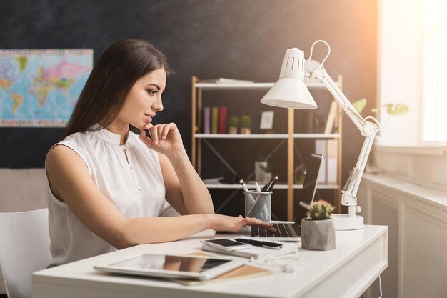 Femme joyeuse tapant sur un ordinateur portable, assise sur son lieu de travail à la maison, espace de copie