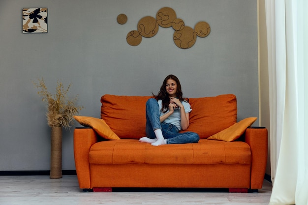 Femme joyeuse avec un téléphone dans les mains sur les appartements du canapé