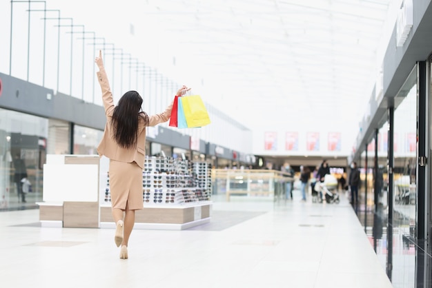 Une femme joyeuse tient au sommet de sacs en papier avec des achats dans un centre commercial