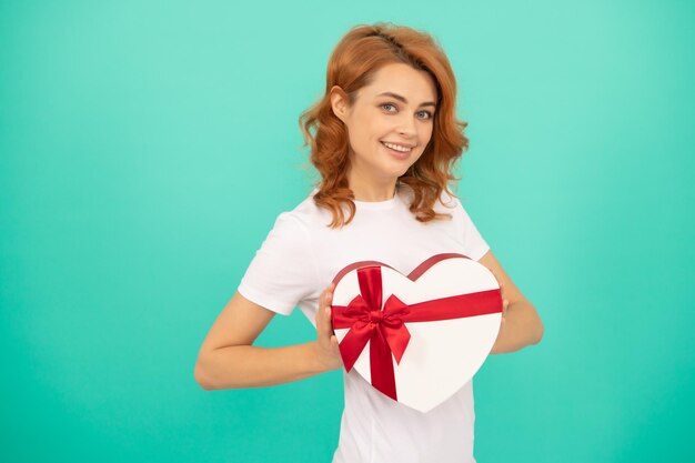 Une femme joyeuse tient une boîte cadeau coeur sur fond bleu