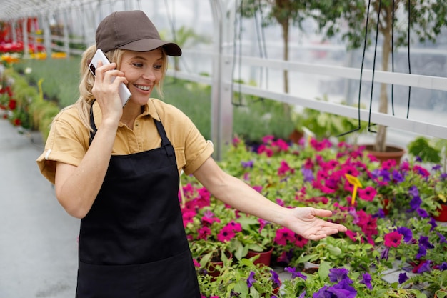 Femme joyeuse en uniforme de fleuriste ayant une conversation avec un client sur un smartphone