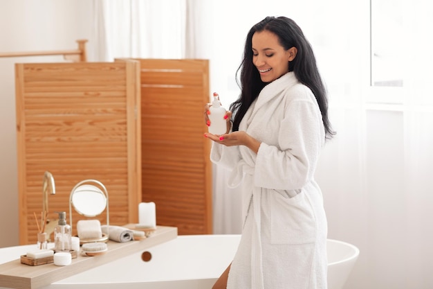 Femme joyeuse utilisant une lotion pour le corps bénéficiant d'une routine de beauté dans la salle de bain