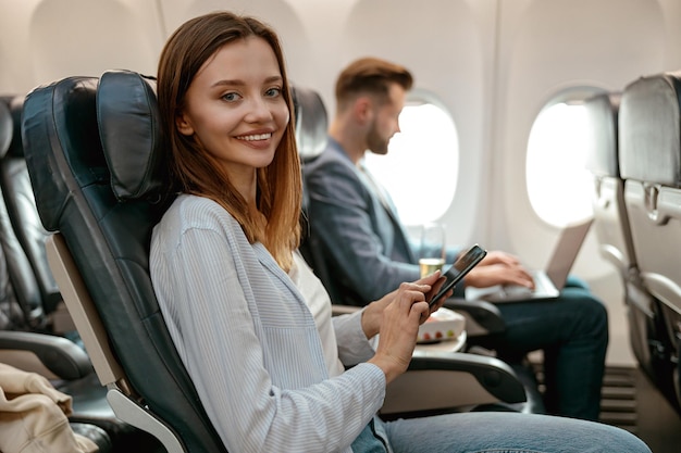 Femme joyeuse utilisant un téléphone portable dans un avion de passagers