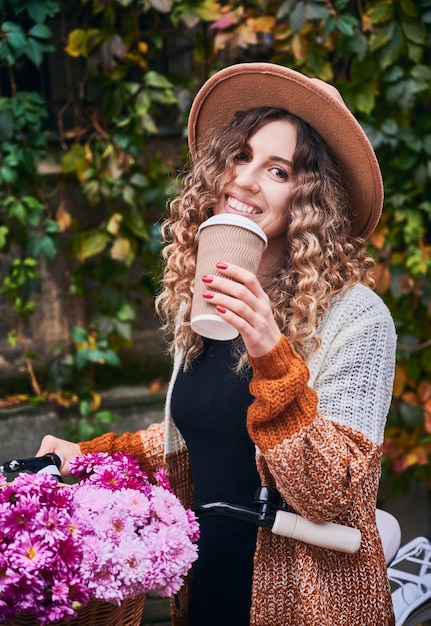 Femme joyeuse avec vélo buvant du café dans la rue