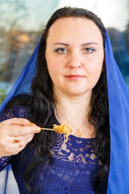 Une femme juive avec sa tête couverte d'une cape bleue à la table du Seder de Pessah mange haroset