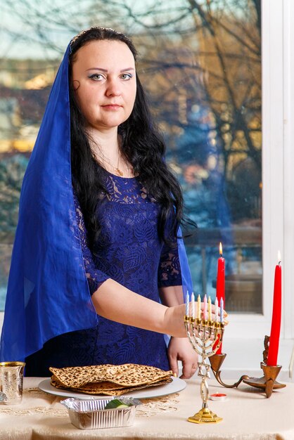 Photo une femme juive avec une tête couverte d'une cape bleue à la table du seder de la pâque allume une bougie