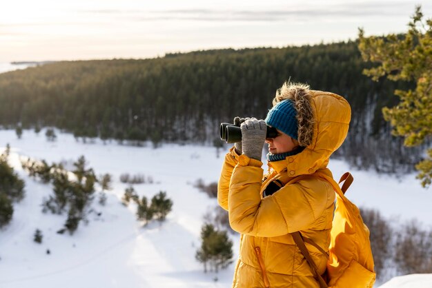 Photo femme avec des jumelles sur la montagne contre l'hiver forêt de rivière enneigée observation des oiseaux espace de copie