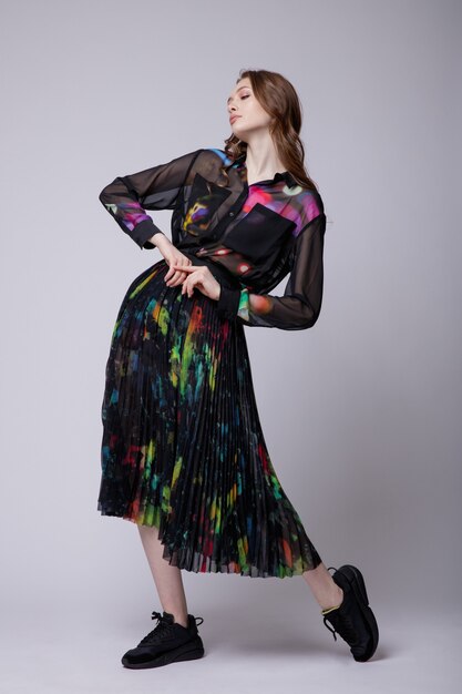 Femme en jupe longue noire et chemise avec des baskets à motifs colorés sur fond blanc Studio Shot