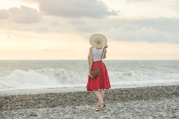 Femme, jupe rouge, chapeau, debout, bord mer, coucher soleil Vue arrière