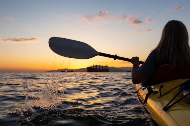 Une femme sur un kayak pagaie dans l'océan pendant un coucher de soleil vibrant