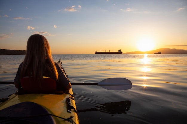 Une femme sur un kayak pagaie dans l'océan pendant un coucher de soleil vibrant