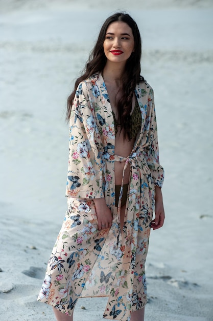 Une femme en kimono fleuri se tient sur une plage.