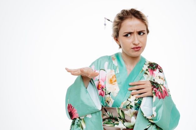 Femme en kimono japonais traditionnel regardant de côté avec une expression dégoûtée faisant un geste d'arrêt levant les mains sur blanc