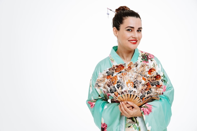 Femme en kimono japonais traditionnel tenant un ventilateur de main heureux et joyeux souriant largement sur blanc
