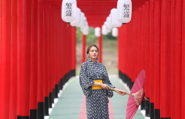 Une Femme En Kimono Tenant Un Parapluie Entrant Dans Le Sanctuaire, Dans Le Jardin Japonais.