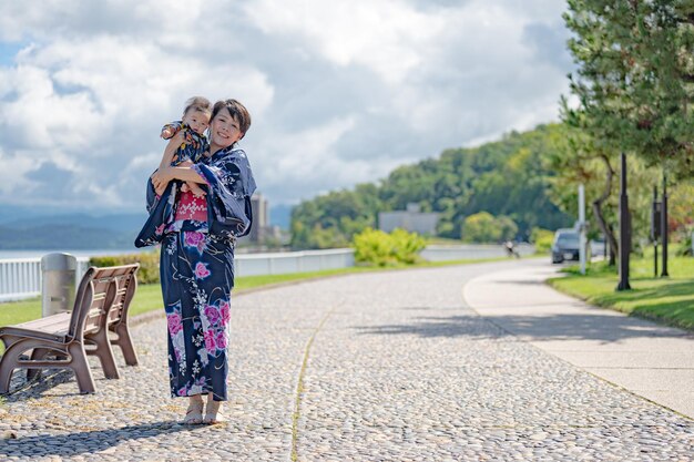 Une femme en kimono tient un enfant sur un trottoir.